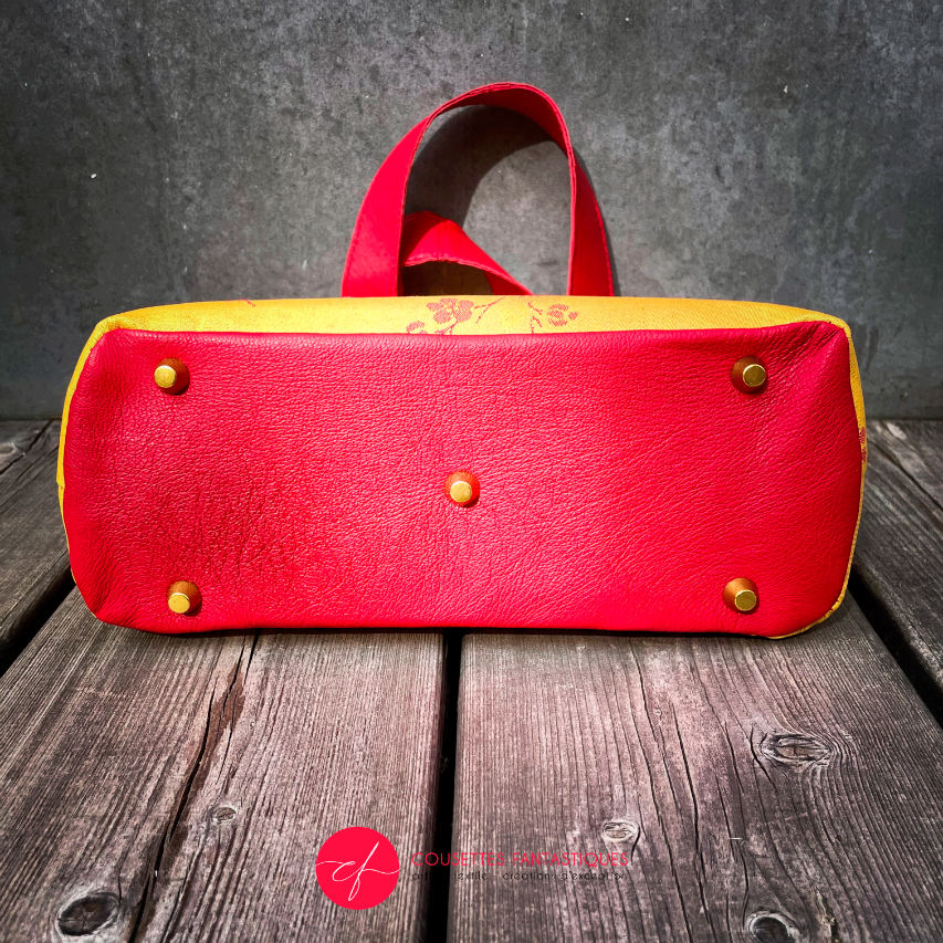 A mini handbag made of yellow upholstery fabric with a red cherry blossom pattern and red leather.