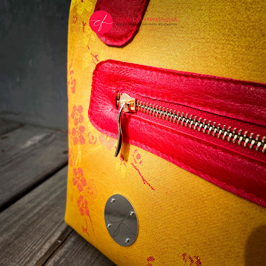 A mini handbag made of yellow upholstery fabric with a red cherry blossom pattern and red leather.