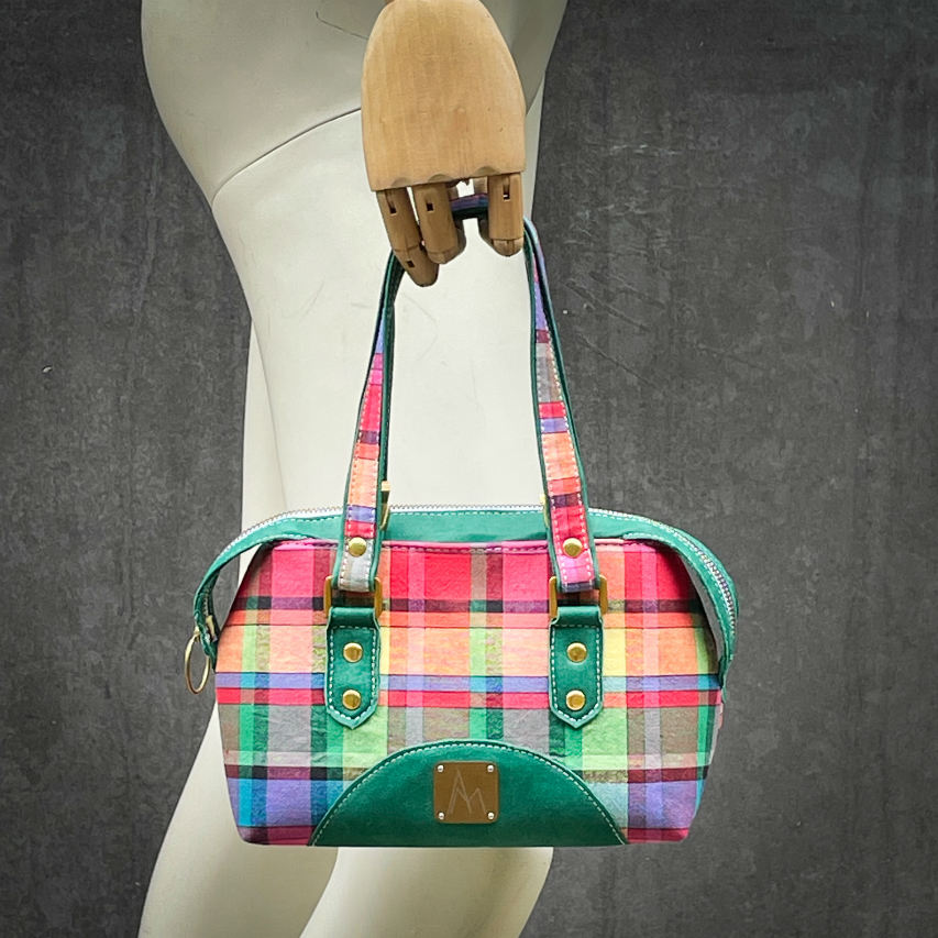 A wallet bag made of forest green leather and multicolored madras fabric.