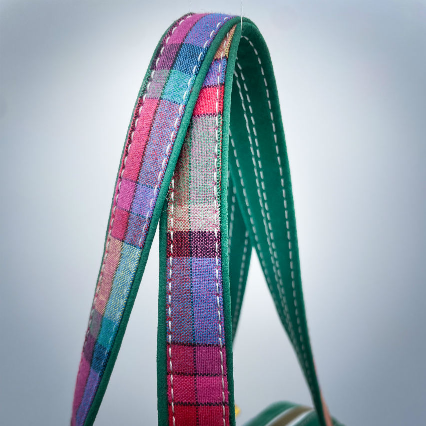 A wallet bag made of forest green leather and multicolored madras fabric.