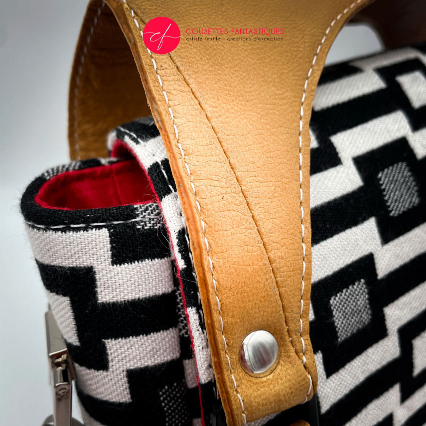 A handbag made of black and white babywearing fabric with a geometric pattern, caramel leather, and red poplin.