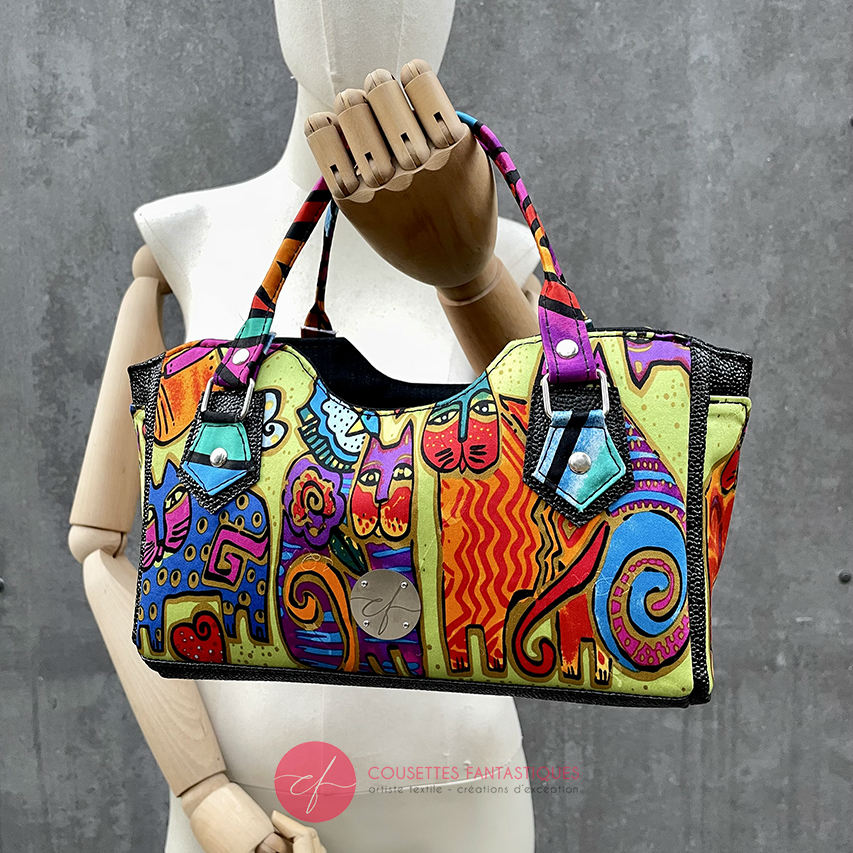 A small handbag made of shiny black faux galuchat texture and a silk scarf with a very colorful cat motif.