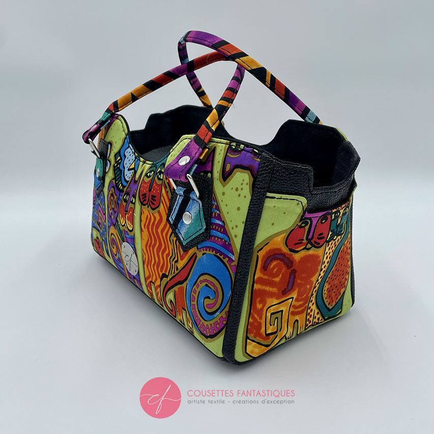 A small handbag made of shiny black faux galuchat texture and a silk scarf with a very colorful cat motif.