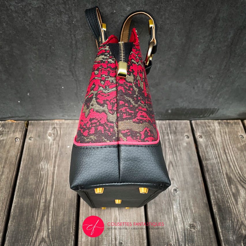 A handbag made of black, gold, and red faux leather and a scarf fabric in the same tones, with a marbled pattern.