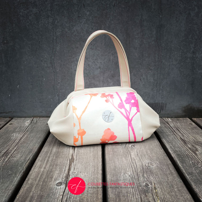 A handbag made of cream synthetic upholstery fabric and cream faux leather, featuring a gradient botanical pattern from pink to orange.