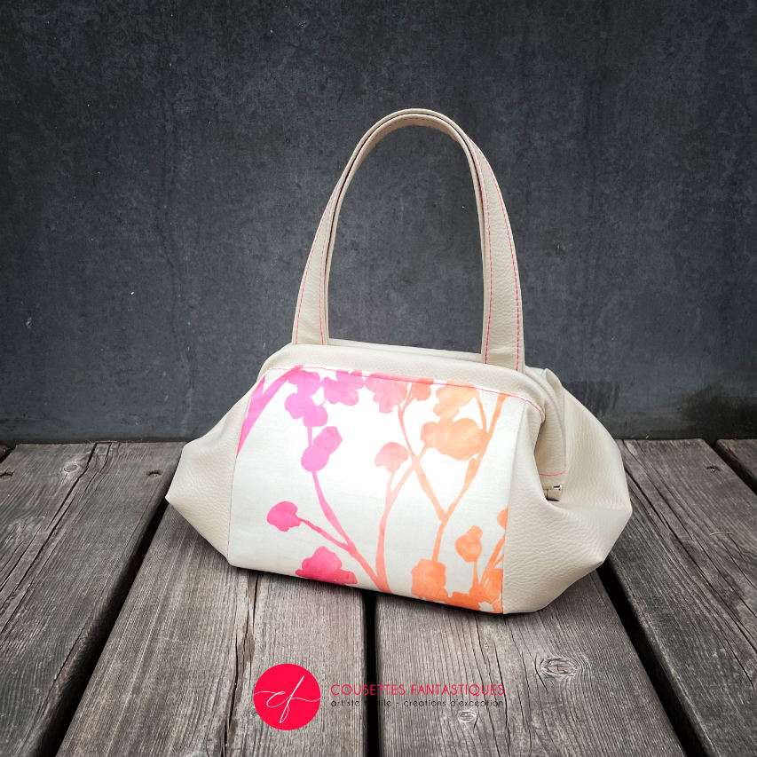 A handbag made of cream synthetic upholstery fabric and cream faux leather, featuring a gradient botanical pattern from pink to orange.