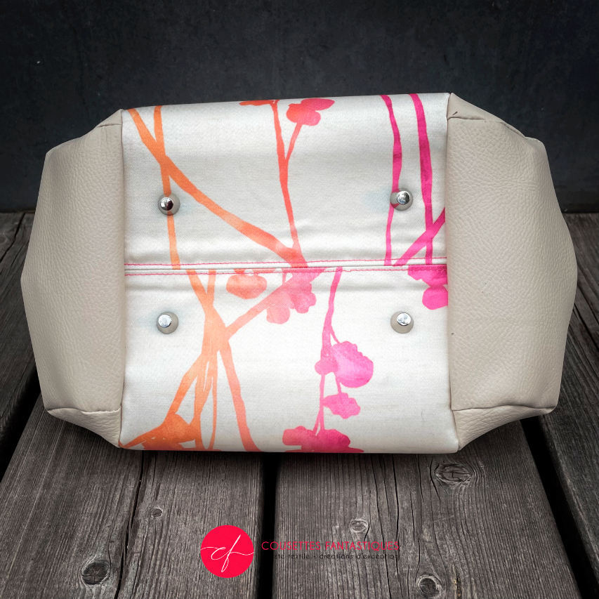 A handbag made of cream synthetic upholstery fabric and cream faux leather, featuring a gradient botanical pattern from pink to orange.