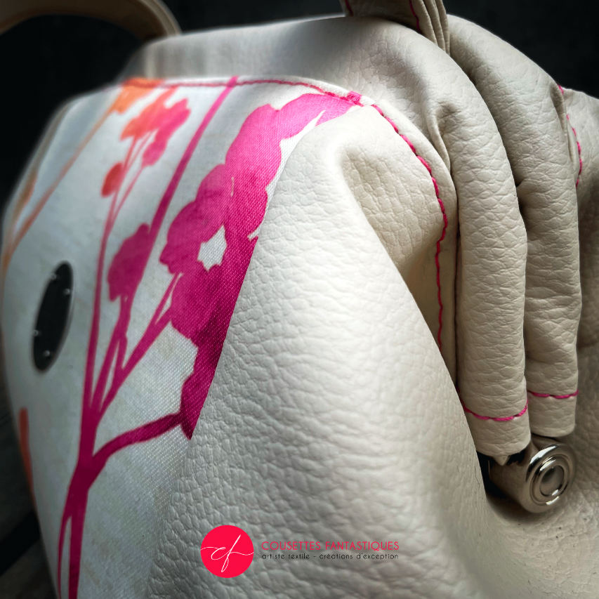 A handbag made of cream synthetic upholstery fabric and cream faux leather, featuring a gradient botanical pattern from pink to orange.