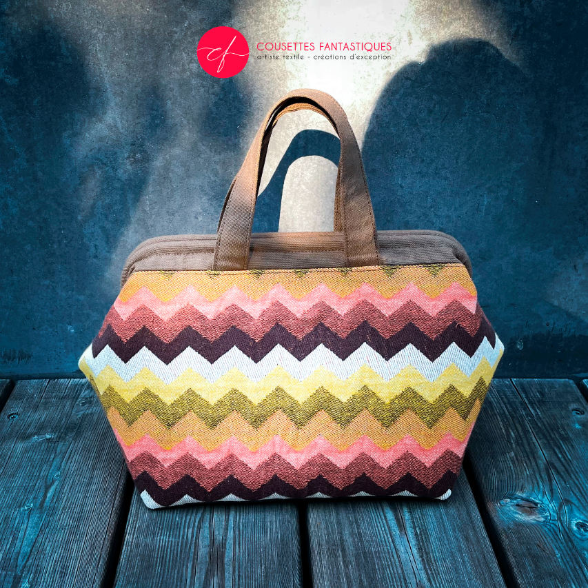 A handbag made of wrap fabric with a giant chevron pattern in autumn tones (pink, brown, orange, yellow, and white).