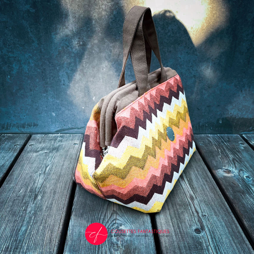 A handbag made of wrap fabric with a giant chevron pattern in autumn tones (pink, brown, orange, yellow, and white).