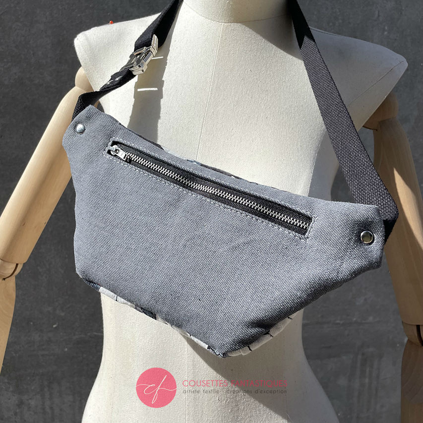 A fanny pack made from babywearing fabric in gray, white, and blue tones with a floral and geometric pattern and gray denim.