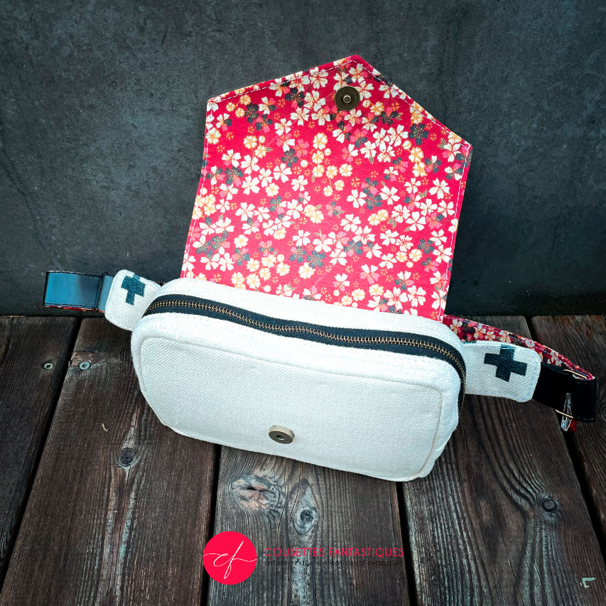 A fanny pack made from coarse ecru canvas with a black geometric pattern of plus signs and a flowery poplin in red, black, white, and yellow tones.