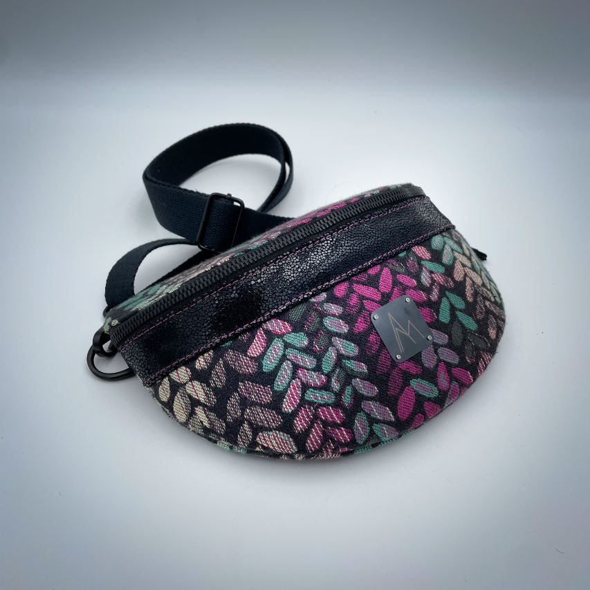 A fanny pack sewn from black patent leather and a scrap of baby wrap fabric with a pattern of green, beige, and pink stitches on a black background, paired with bright pink poplin lining inside.