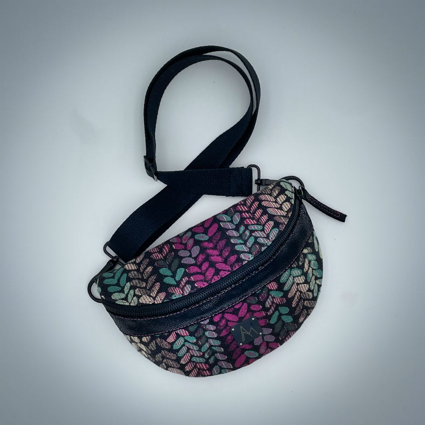 A fanny pack sewn from black patent leather and a scrap of baby wrap fabric with a pattern of green, beige, and pink stitches on a black background, paired with bright pink poplin lining inside.