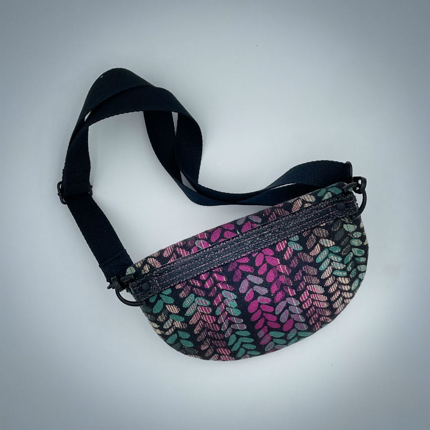 A fanny pack sewn from black patent leather and a scrap of baby wrap fabric with a pattern of green, beige, and pink stitches on a black background, paired with bright pink poplin lining inside.