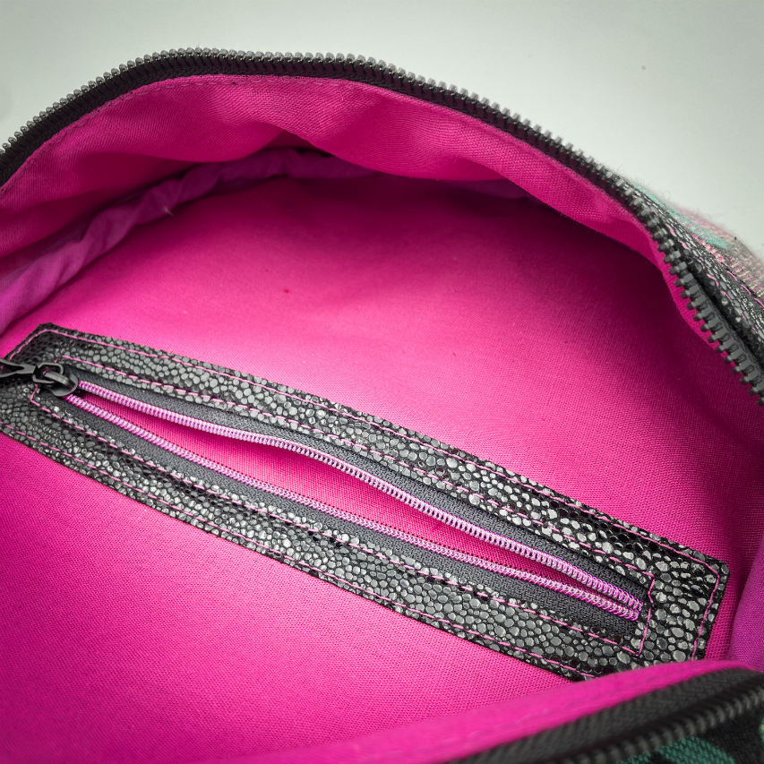 A fanny pack sewn from black patent leather and a scrap of baby wrap fabric with a pattern of green, beige, and pink stitches on a black background, paired with bright pink poplin lining inside.