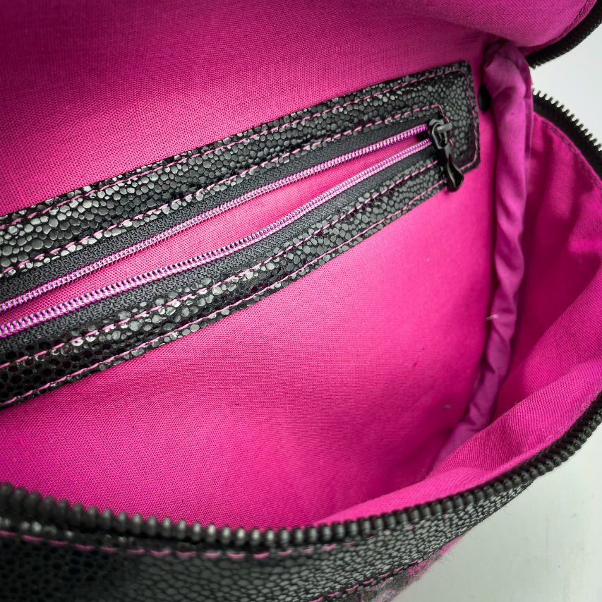 A fanny pack sewn from black patent leather and a scrap of baby wrap fabric with a pattern of green, beige, and pink stitches on a black background, paired with bright pink poplin lining inside.