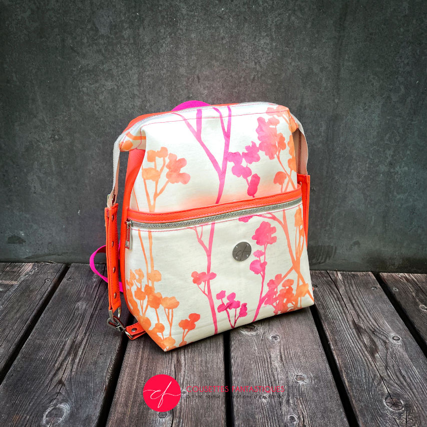 A backpack made with bright orange synthetic leather and cream upholstery fabric with a gradient of plant patterns from pink to orange.