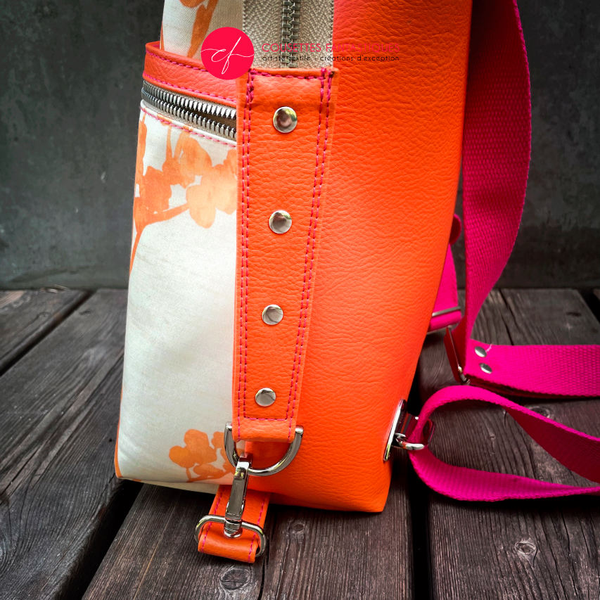 A backpack made with bright orange synthetic leather and cream upholstery fabric with a gradient of plant patterns from pink to orange.