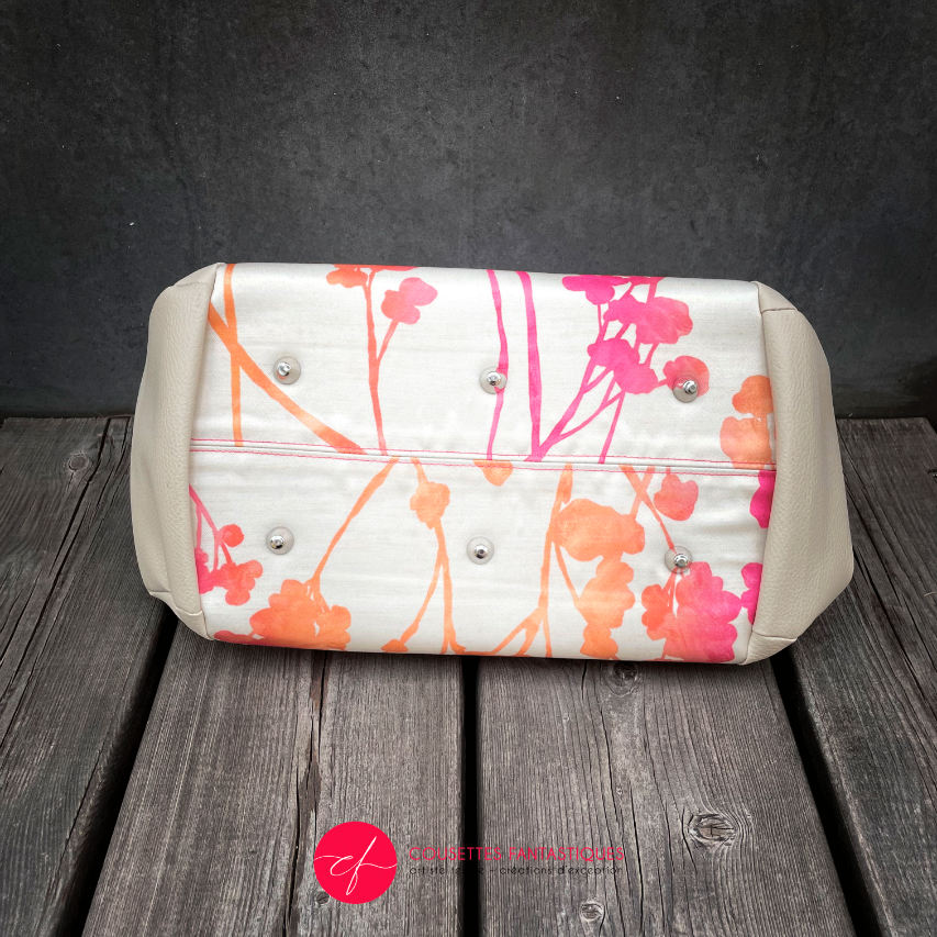A small handbag made of cream synthetic upholstery fabric with a botanical pattern that fades from pink to orange.