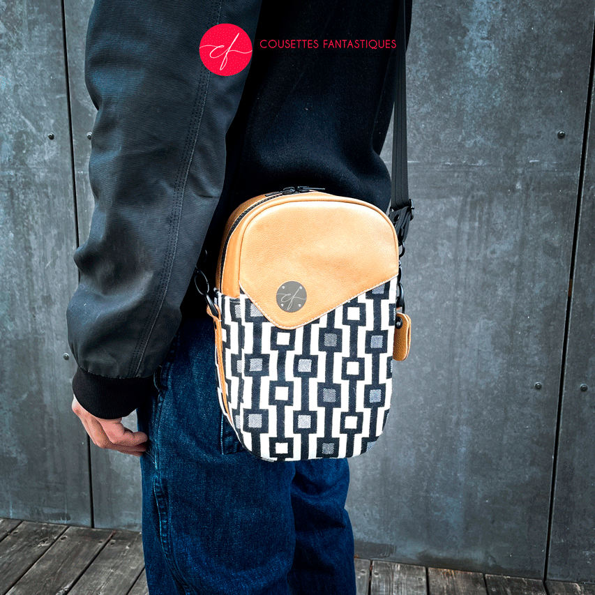 A messenger bag made from a black and white geometric pattern babywearing wrap, caramel leather, and red poplin.