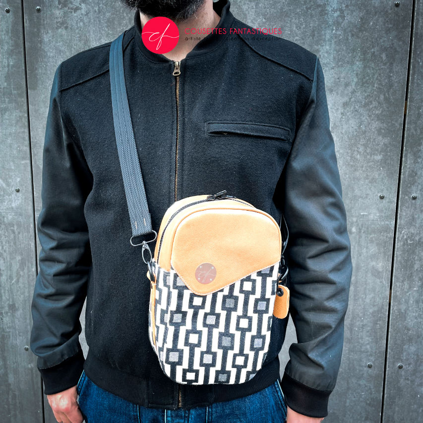 A messenger bag made from a black and white geometric pattern babywearing wrap, caramel leather, and red poplin.