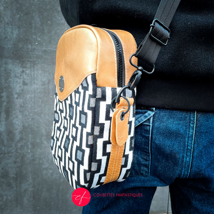 A messenger bag made from a black and white geometric pattern babywearing wrap, caramel leather, and red poplin.
