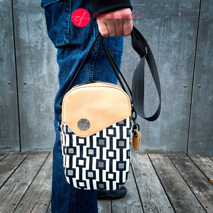 A messenger bag made from a black and white geometric pattern babywearing wrap, caramel leather, and red poplin.