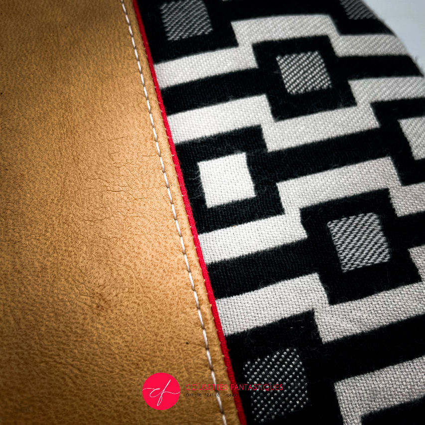 A messenger bag made from a black and white geometric pattern babywearing wrap, caramel leather, and red poplin.