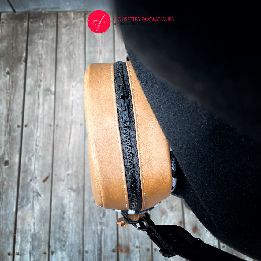 A messenger bag made from a black and white geometric pattern babywearing wrap, caramel leather, and red poplin.