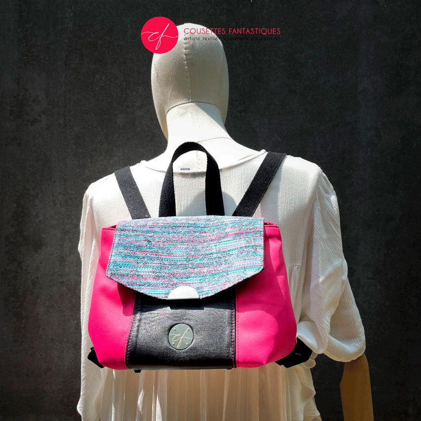 A backpack made with bright pink upholstery fabric, black leather, and wrap fabric with a floral pattern.