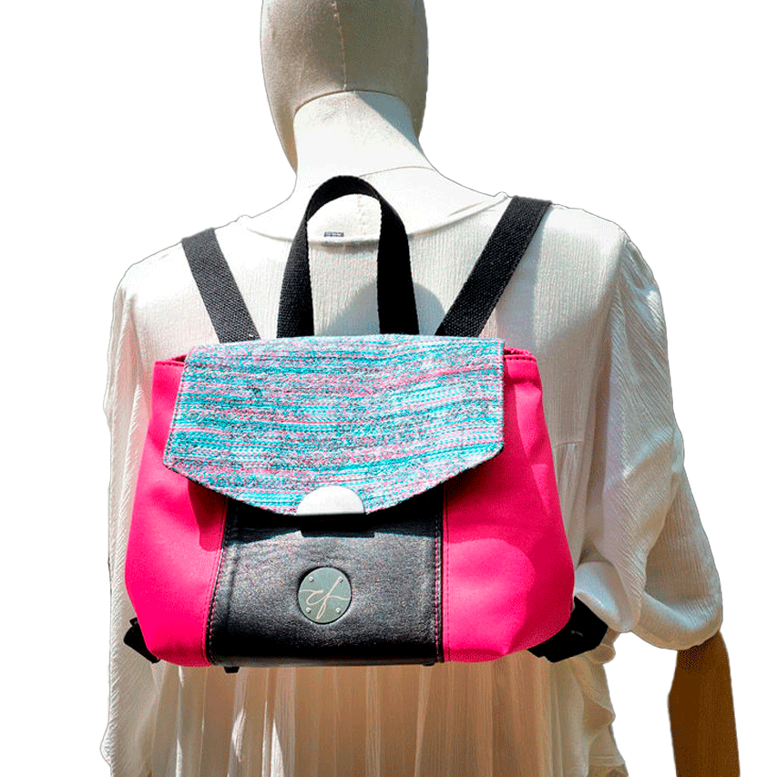 A backpack made with bright pink upholstery fabric, black leather, and wrap fabric with a floral pattern.