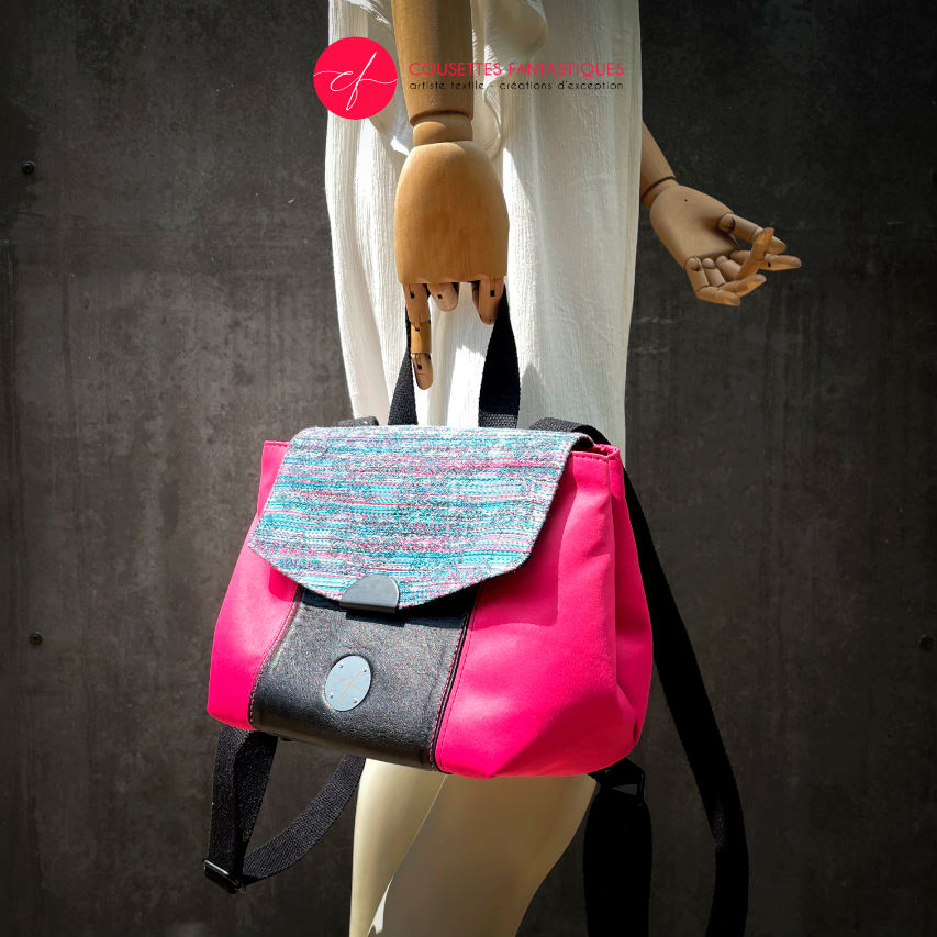 A backpack made with bright pink upholstery fabric, black leather, and wrap fabric with a floral pattern.