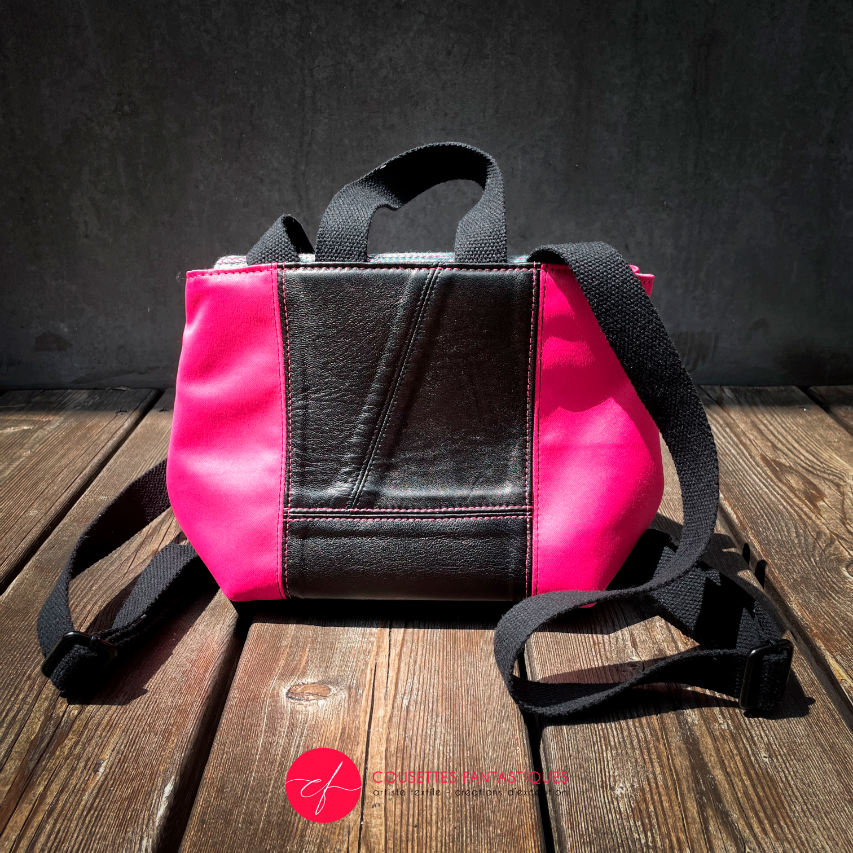 A backpack made with bright pink upholstery fabric, black leather, and wrap fabric with a floral pattern.