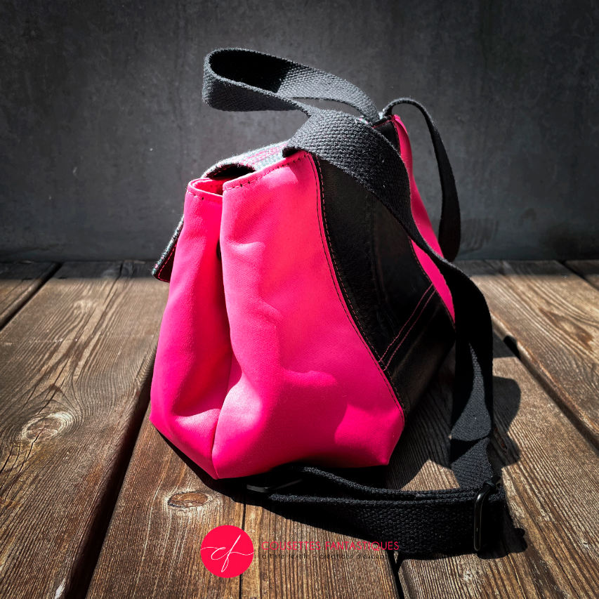 A backpack made with bright pink upholstery fabric, black leather, and wrap fabric with a floral pattern.