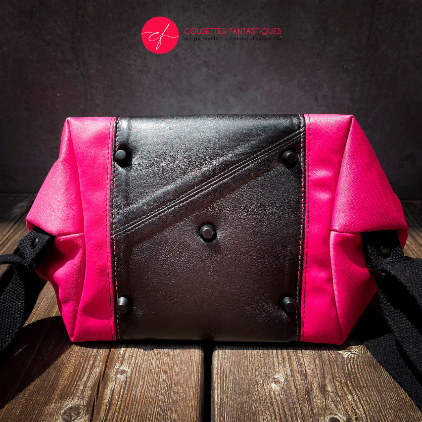 A backpack made with bright pink upholstery fabric, black leather, and wrap fabric with a floral pattern.