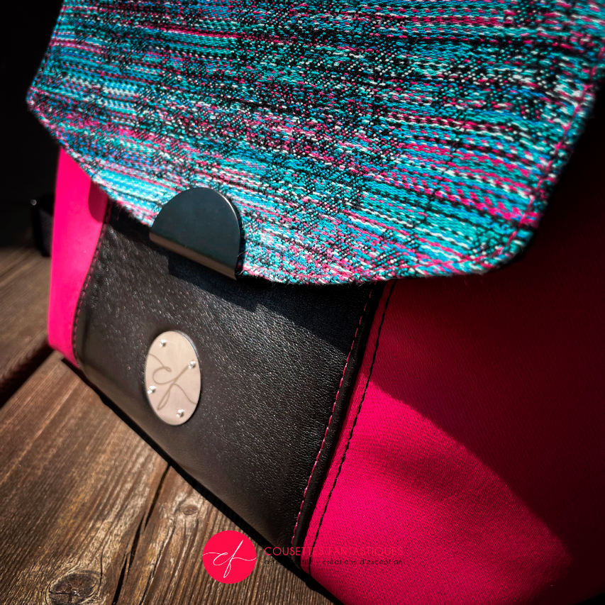 A backpack made with bright pink upholstery fabric, black leather, and wrap fabric with a floral pattern.