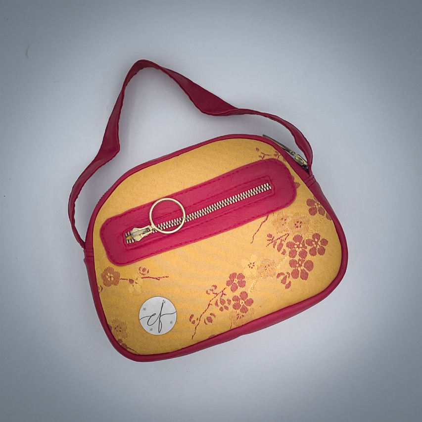 A mini handbag made of yellow upholstery fabric with a red cherry blossom pattern and red leather.