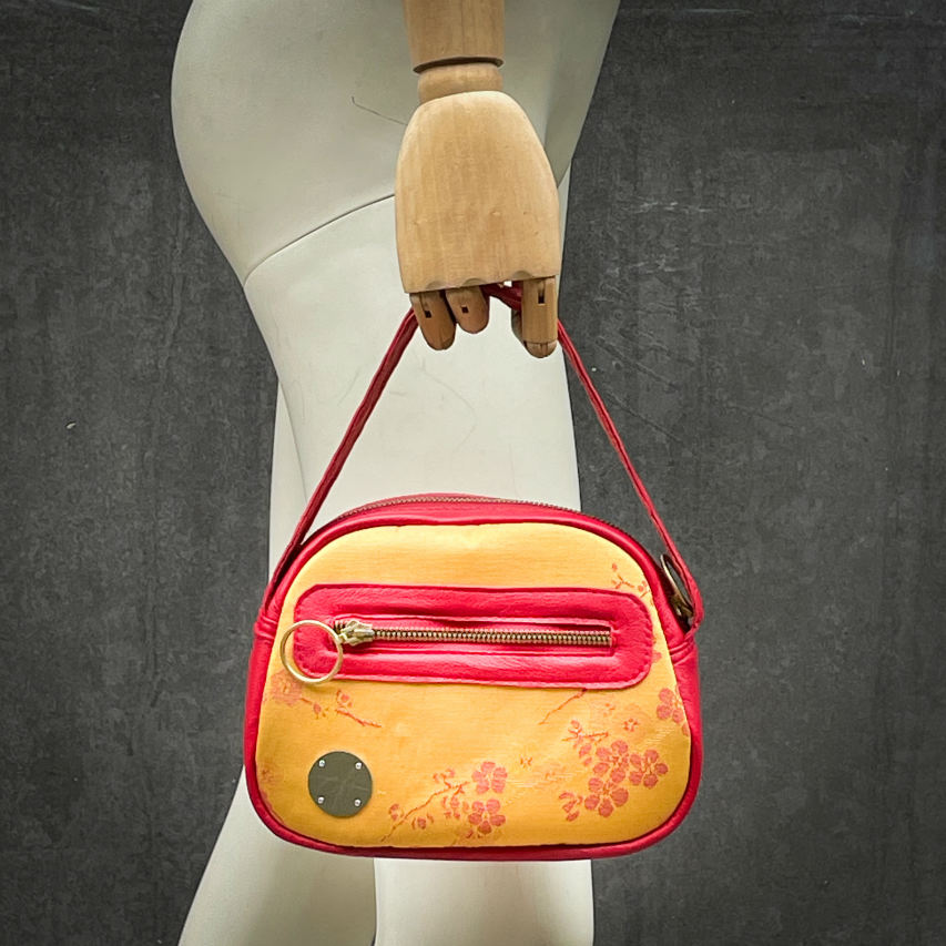 A mini handbag made of yellow upholstery fabric with a red cherry blossom pattern and red leather.