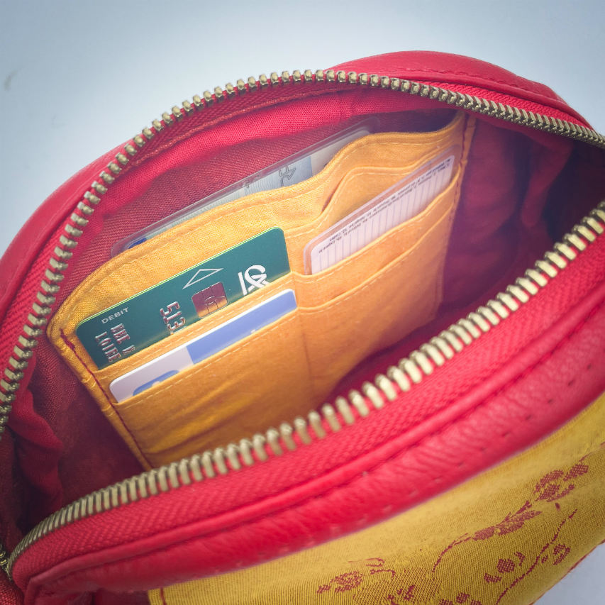 A mini handbag made of yellow upholstery fabric with a red cherry blossom pattern and red leather.