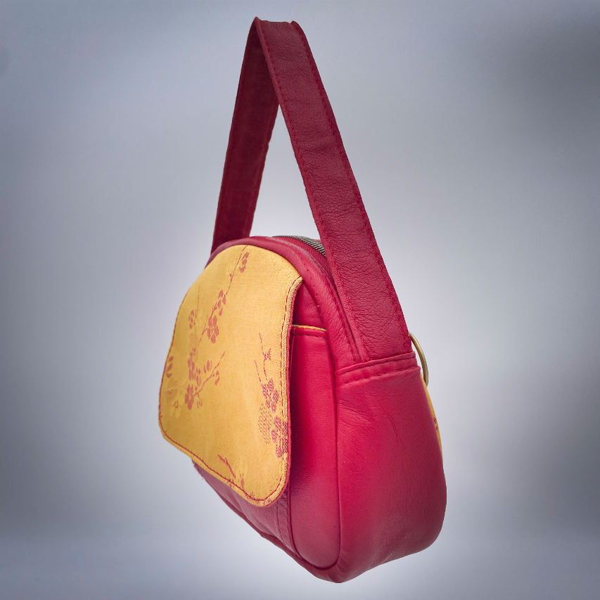 A mini handbag made of yellow upholstery fabric with a red cherry blossom pattern and red leather.