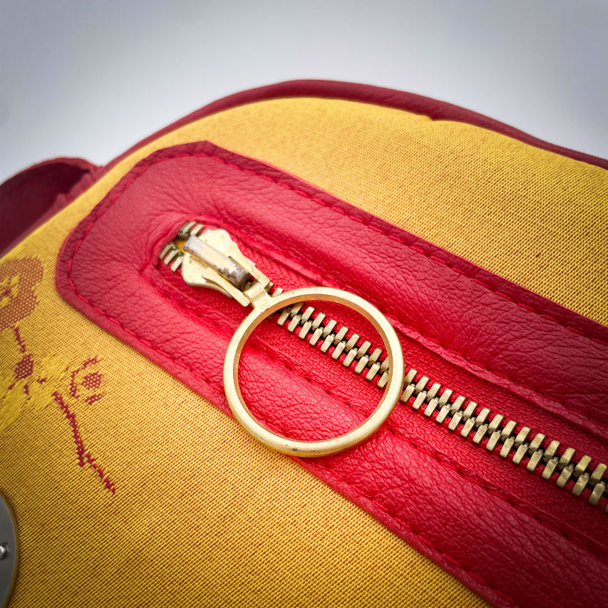 A mini handbag made of yellow upholstery fabric with a red cherry blossom pattern and red leather.