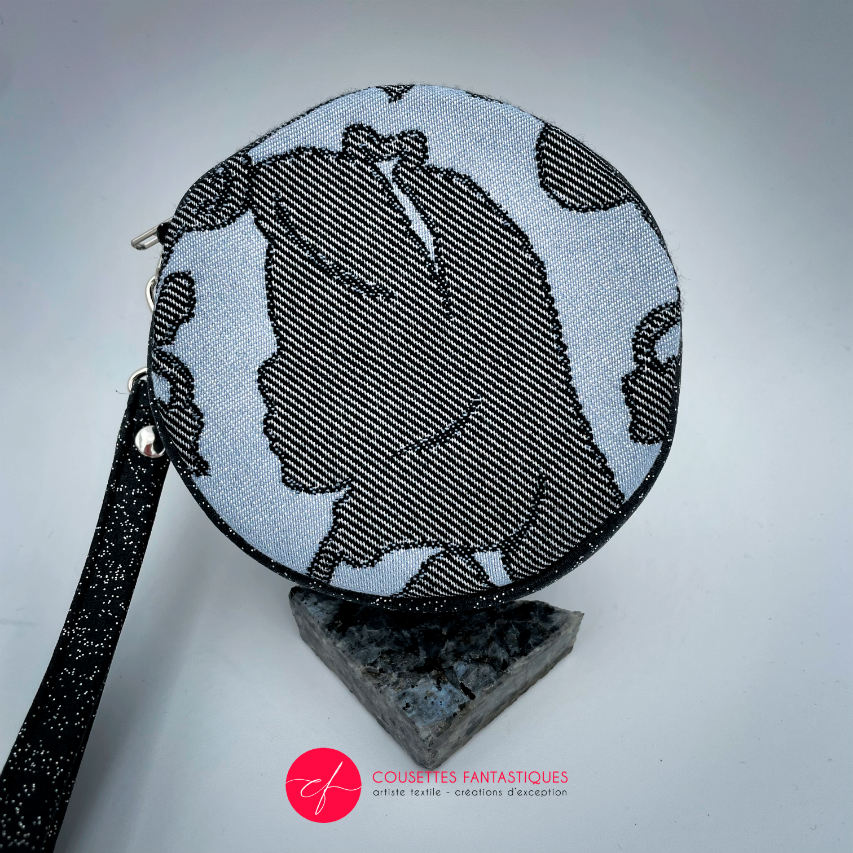 A round pouch made of multicolored glitter canvas and a gray-blue, black, and silver glitter babywearing wrap with a pattern inspired by the “Alice in Wonderland” story.