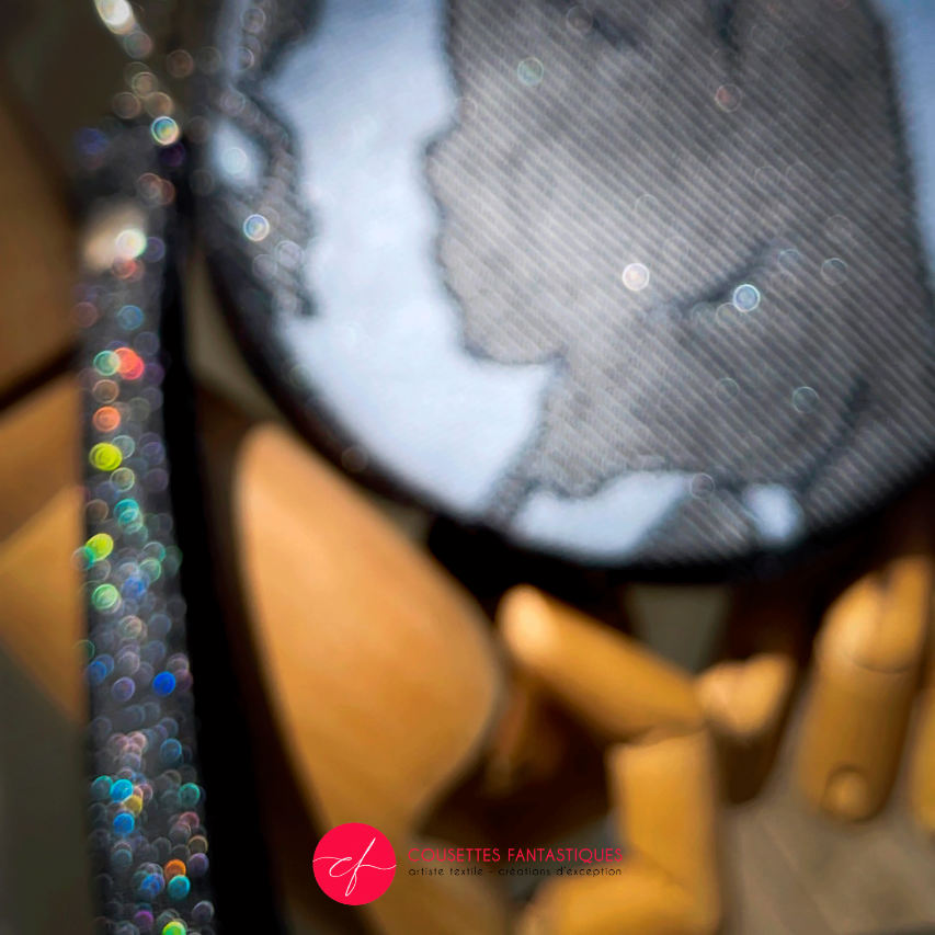 A round pouch made of multicolored glitter canvas and a gray-blue, black, and silver glitter babywearing wrap with a pattern inspired by the “Alice in Wonderland” story.