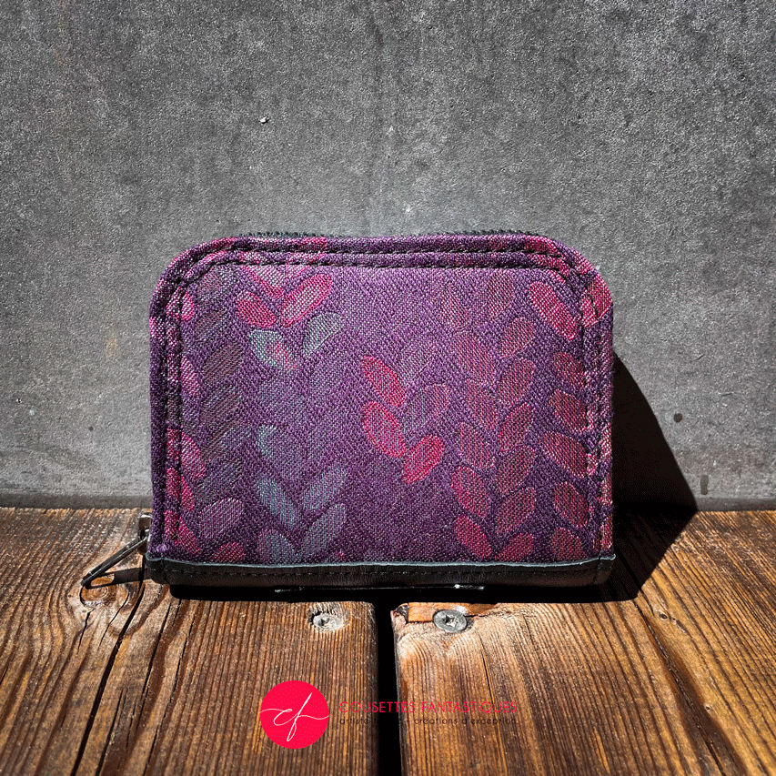 A small zippered card and coin holder made of fabric in shades of purples, crimsons, pinks... with a droplet pattern.