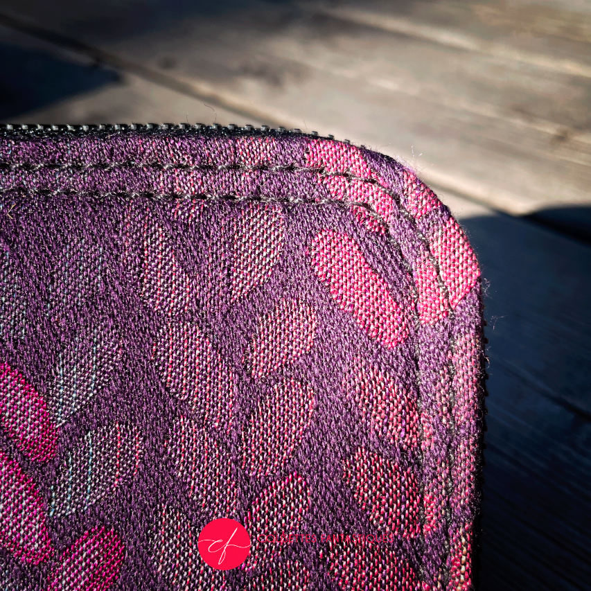 A small zippered card and coin holder made of fabric in shades of purples, crimsons, pinks... with a droplet pattern.