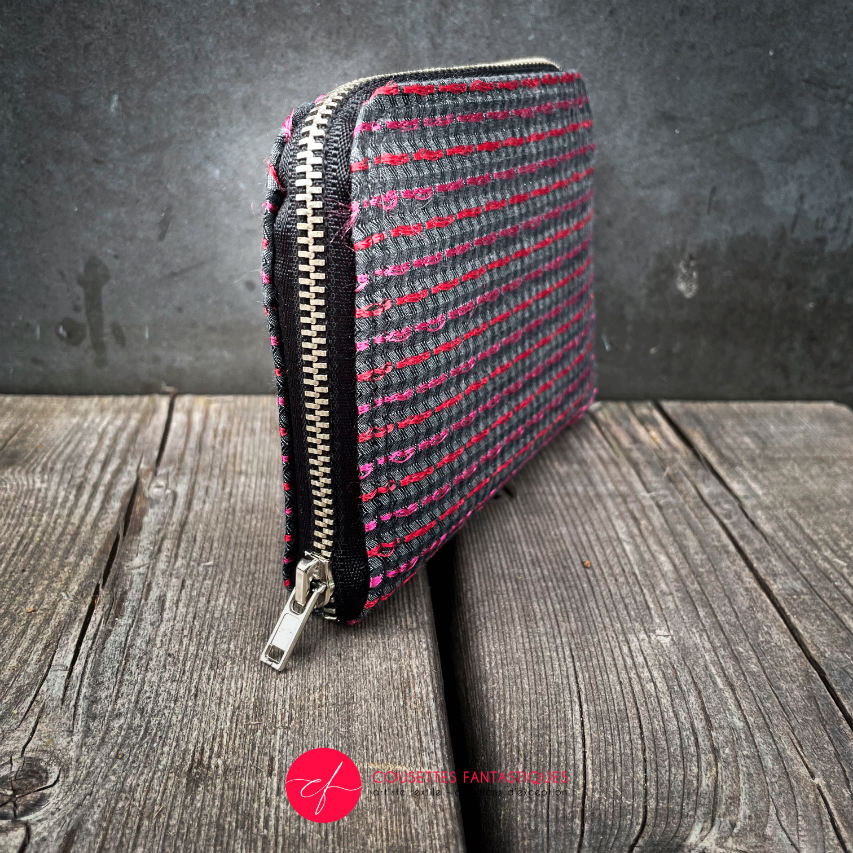 A small zippered card and coin holder made of gray fabric embroidered with shiny pink and red lines, with a textured gray matte interior.