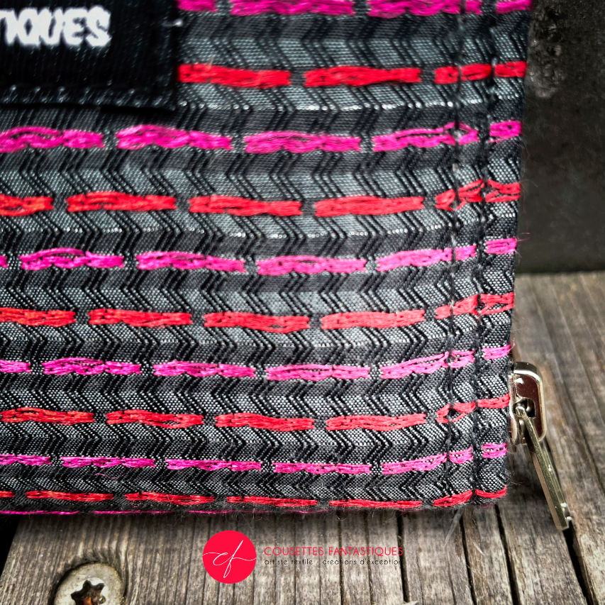 A small zippered card and coin holder made of gray fabric embroidered with shiny pink and red lines, with a textured gray matte interior.