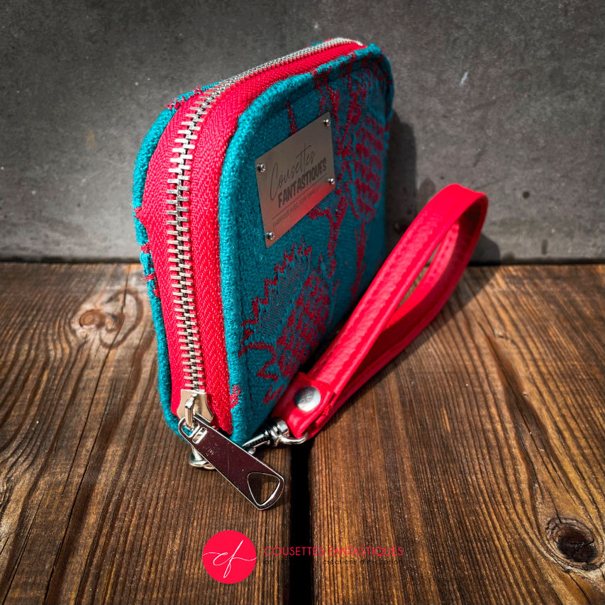 A small zippered card and coin holder made from blood-red and emerald green wrap fabric with thistle patterns and emerald green linen. It comes with a bright red faux leather wrist strap.