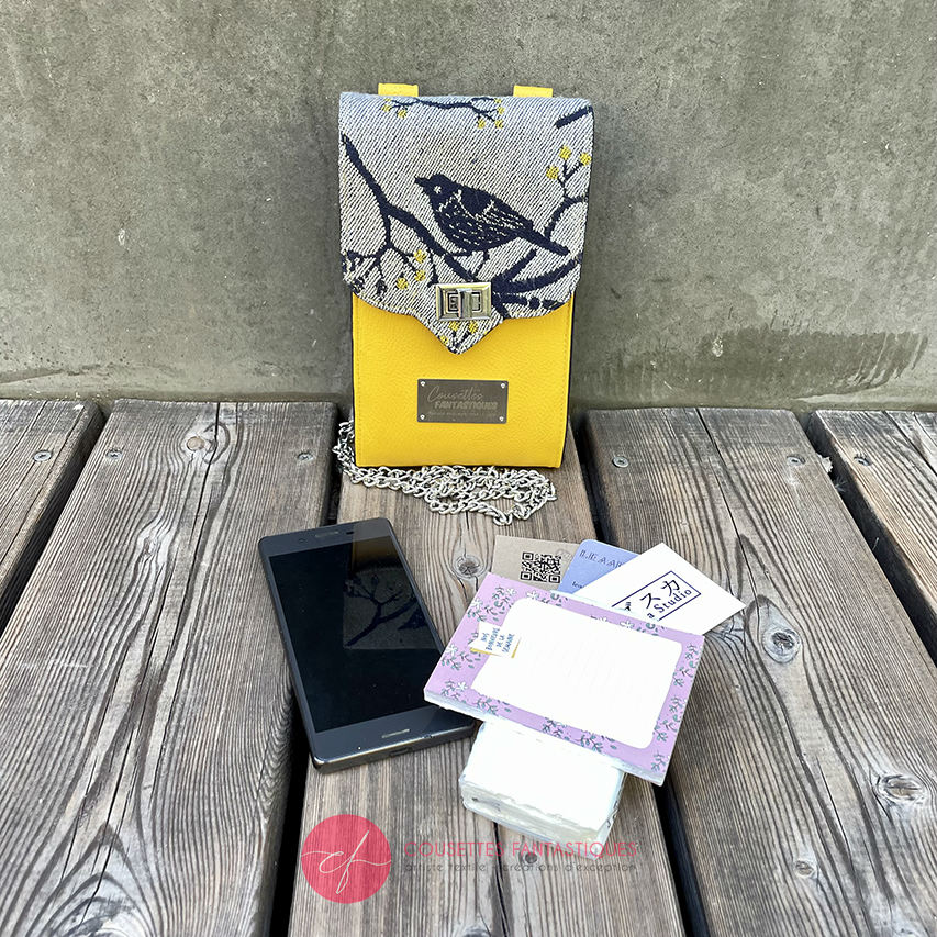 A phone-purse made from a gray, navy blue, and yellow babywearing scarf with bird motifs, and sun-yellow faux leather.